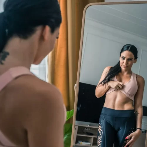 Woman in workout clothes checking her abs in the mirror, focusing on body image and self-reflection